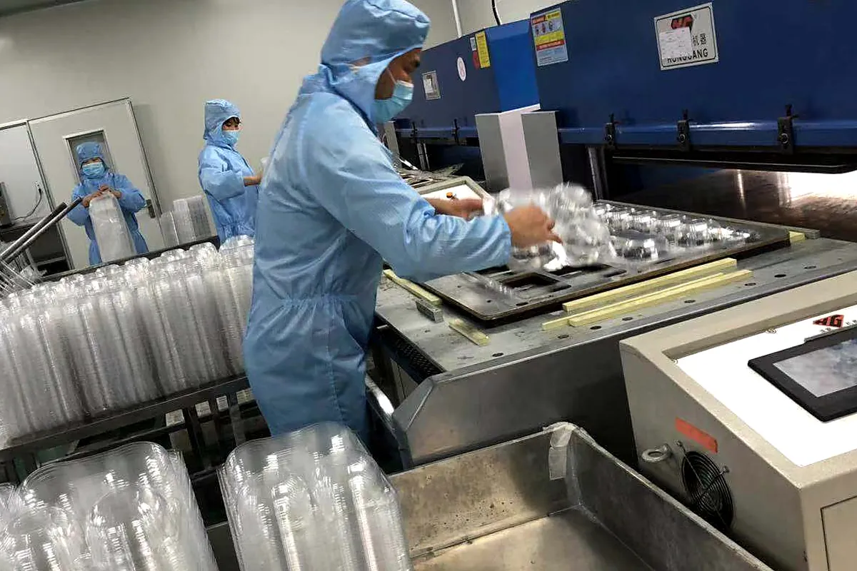 Yinling workers handling newly formed clear food containers beside thermoforming equipment